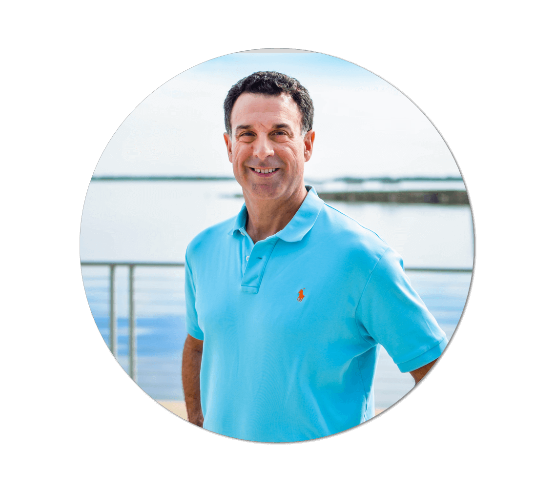 A man in a blue polo shirt smiling in front of a body of water.