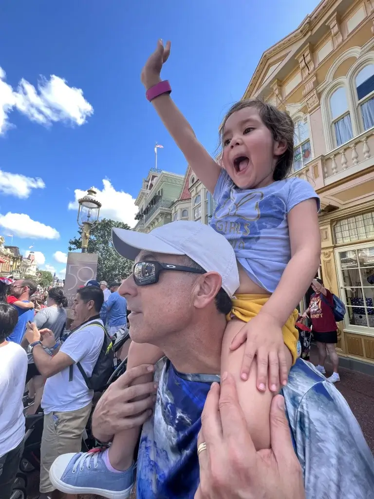 A man is holding a little girl in front of a crowd at disney world.