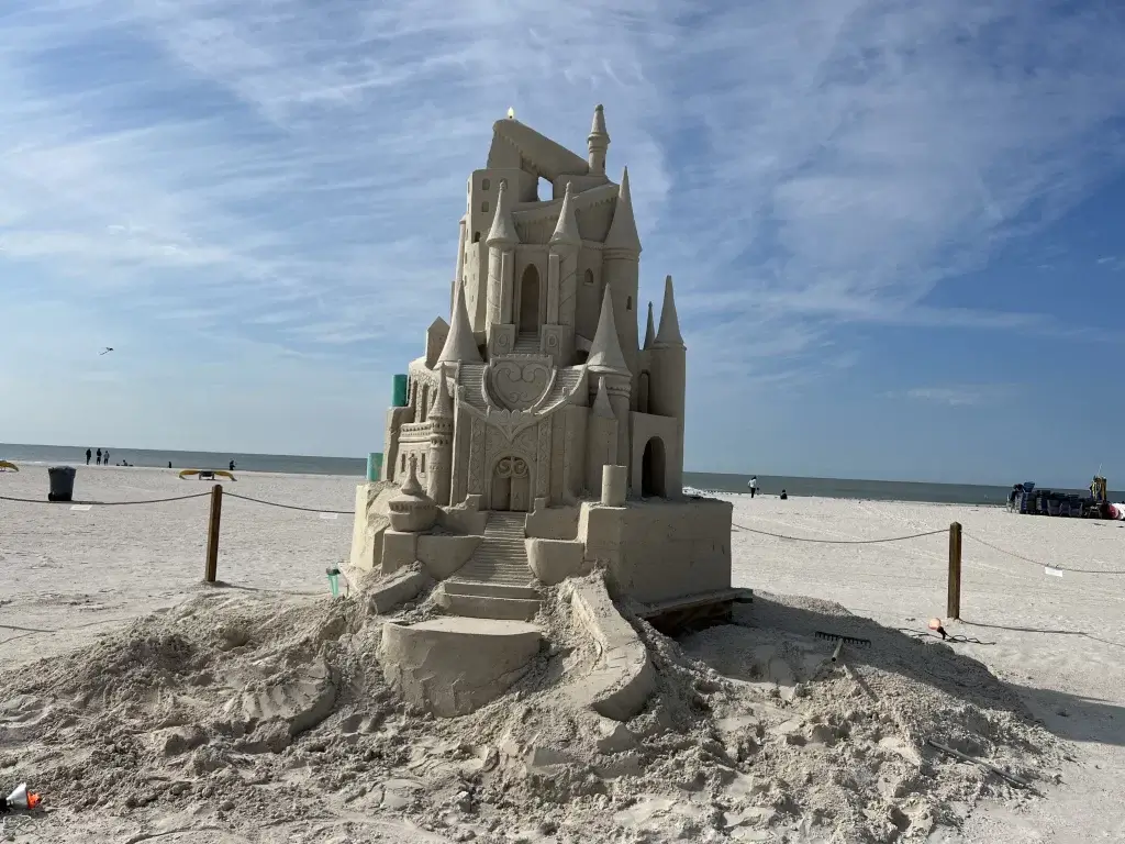 A sand castle on the beach with a castle in the background.