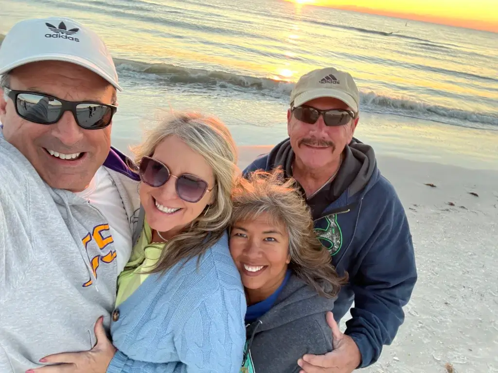 Four people taking a selfie on the beach at sunset.